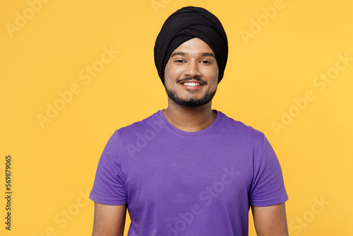 Quadro su tela Smiling cheerful fun happy devotee Sikh Indian man ties his traditional turban dastar wear purple t-shirt looking camera isolated on plain yellow background studio portrait