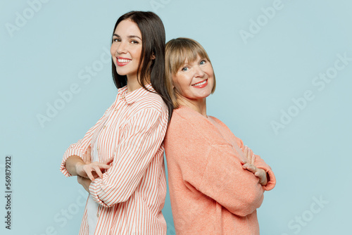 Side view elder parent mom with young adult daughter two women together wearing casual clothes hold hands crossed folded stand back to back isolated on plain blue cyan background. Family day concept. photo