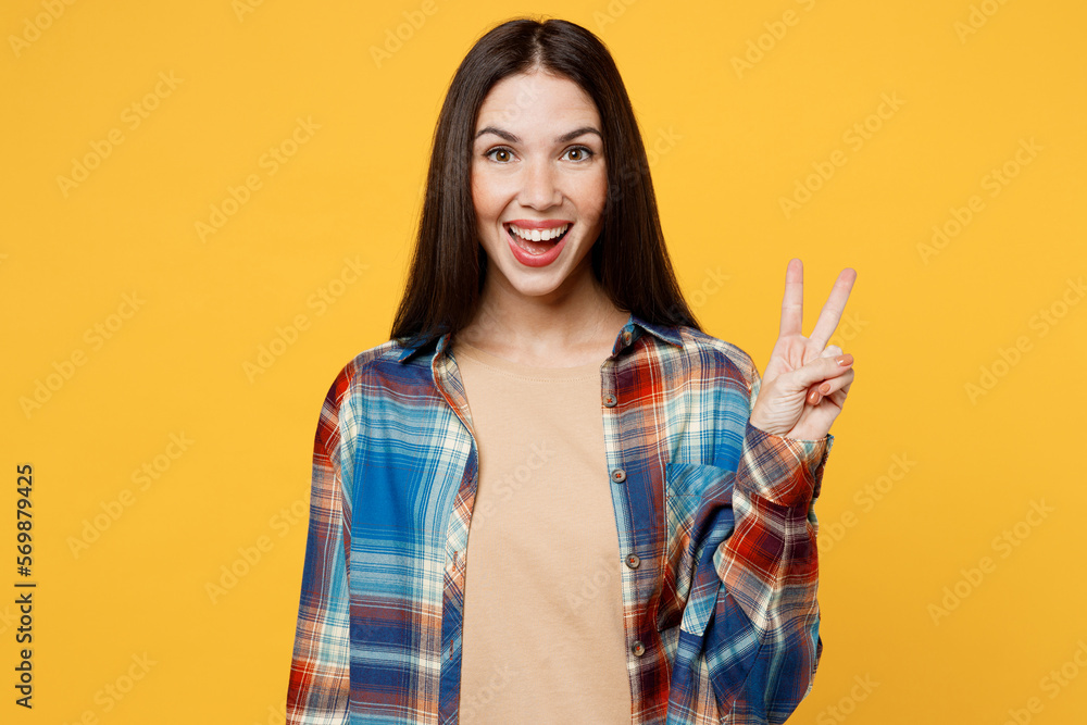 Young cheerful fun cool positive satisfied smiling caucasian woman wearing blue shirt beige t-shirt showing victory sign isolated on plain yellow background studio portrait. People lifestyle concept. Young cheerful fun cool positive satisfied smiling caucasian woman wearing blue shirt beige t-shirt showing victory sign isolated on plain yellow background studio portrait. People lifestyle concept.