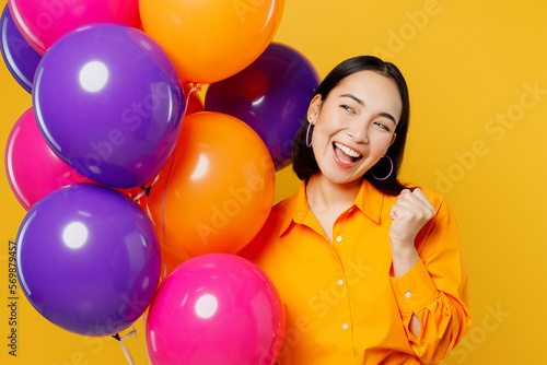 Close up happy fun young woman wear casual clothes celebrating holding look at bunch of colorful air balloons do winner gesture isolated on plain yellow background Birthday 8 14 holiday party concept © ViDi Studio