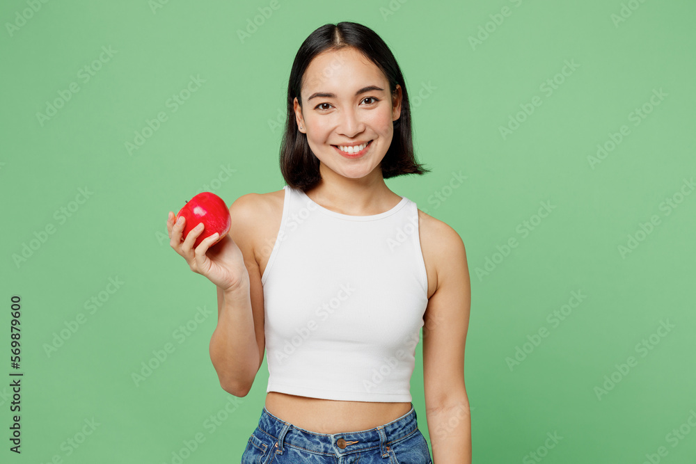 Young smiling vegetarian woman wear white clothe s hold in hand ripe red apple look camera isolated on plain pastel light green background. Proper nutrition healthy fast food unhealthy choice concept. Young smiling vegetarian woman wear white clothe s hold in hand ripe red apple look camera isolated on plain pastel light green background. Proper nutrition healthy fast food unhealthy choice concept.