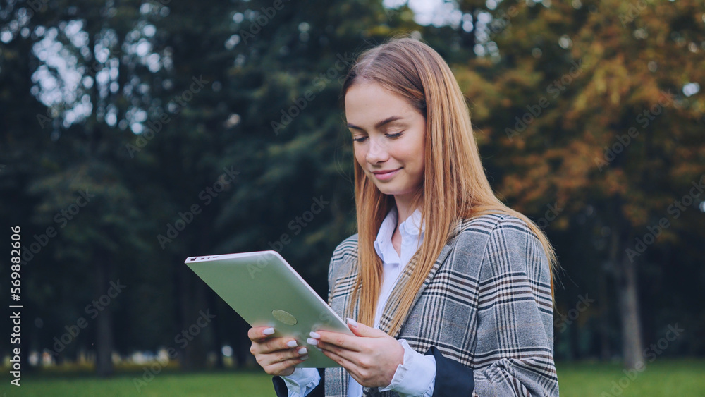 Obraz premium A young girl walks with a tablet in the park.