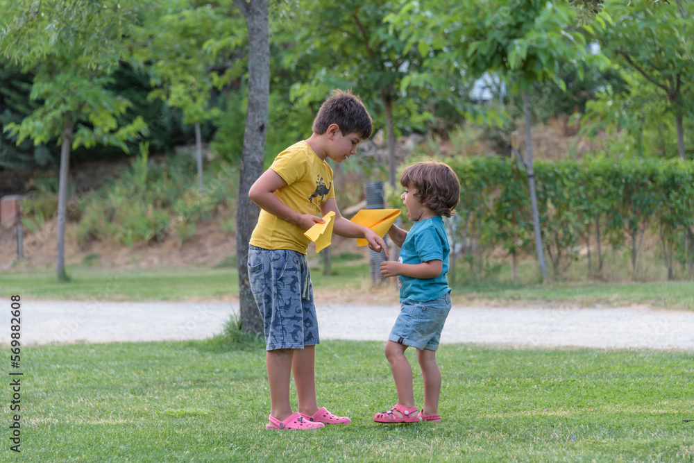 Two little kids playing with cardboard toy airplane in the park at the day time. Concept of happy game. Child having fun outdoors. Two little kids playing with cardboard toy airplane in the park at the day time. Concept of happy game. Child having fun outdoors.