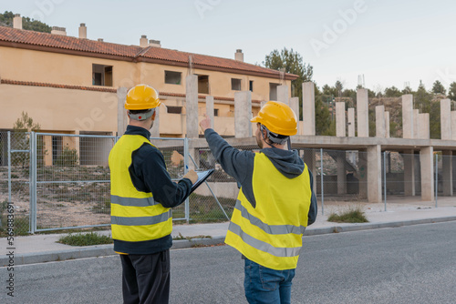 Operarios de obra irreconocibles, señalando, apuntando y mirando el edificio en construcción. 