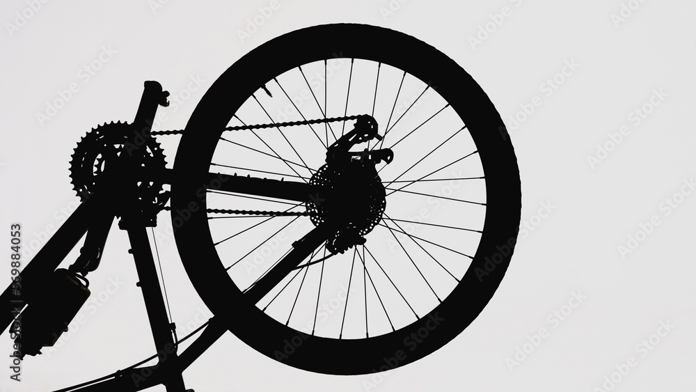 Black silhouette of a part of a modern sports bike on a white isolated background. Close up of a round bicycle wheel with nipple, spokes and brake. Bicycle frame with pedals, chain, sprockets.