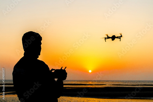 Silhouette of a drone pilot operating a drone standing by the sea at evening sunset. Silhouette view of a drone pilot.