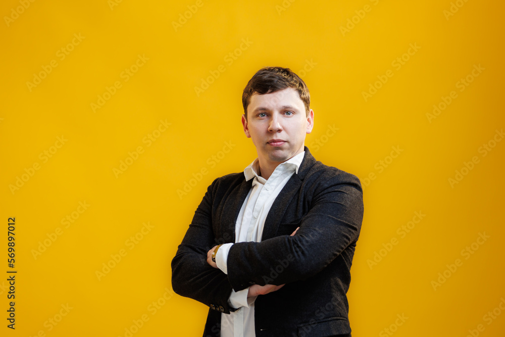 Fototapeta premium Portrait of handsome businessman with crossing hands standing on yellow studio background and looking at camera
