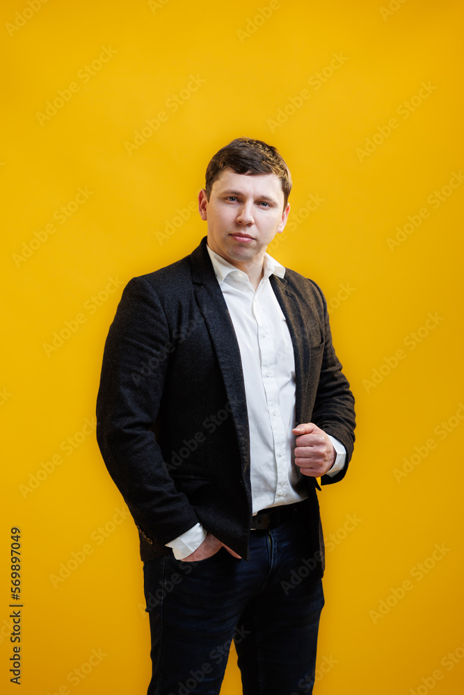 Portrait of focused businessman wearing suit standing on yellow studio background and looking at camera Portrait of focused businessman wearing suit standing on yellow studio background and looking at camera
