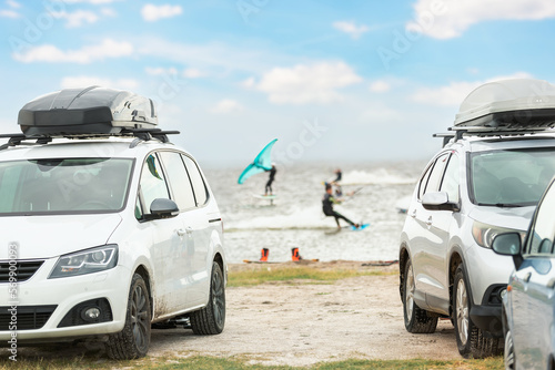 Front view many cars parked with surf board kite equipment on sand beach, van vehicle with rooftop box ocean sea beach watersport spot camp. Adventure travel water sport acitivity