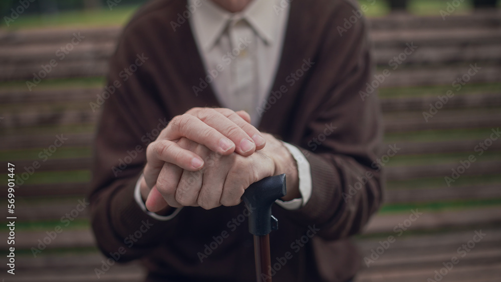 Lonely senior man with walking cane sitting on bench, close-up of wrinkled hands