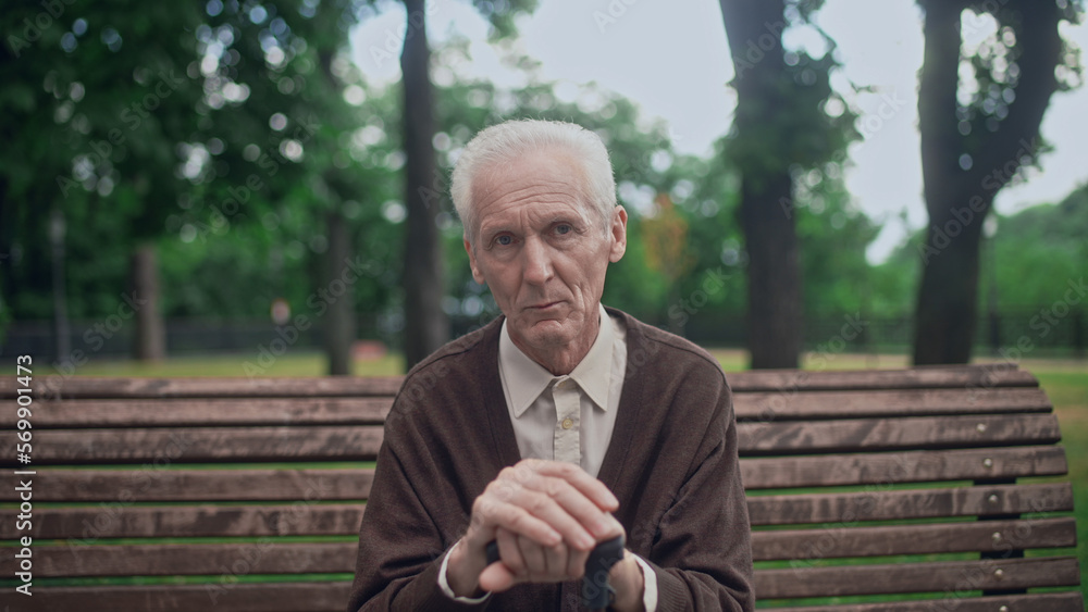 Upset wrinkled senior man sitting in city park alone, holding walking cane Upset wrinkled senior man sitting in city park alone, holding walking cane