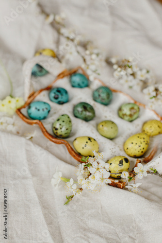 Happy Easter! Stylish easter eggs and blooming spring flowers on rustic table. Natural painted quail eggs in tray and cherry blossoms on linen fabric. Rustic easter still life