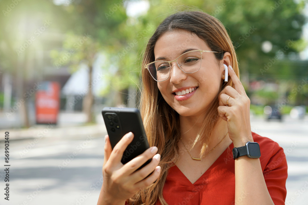 Close-up of goggles girl turns on wireless earphones for listening to music choosing playlist on smartphone outdoor in the morning Close-up of goggles girl turns on wireless earphones for listening to music choosing playlist on smartphone outdoor in the morning