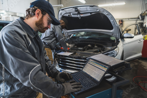 Serviceman making car diagnostics with a laptop in a workshop , his colleague working in the background. High quality photo