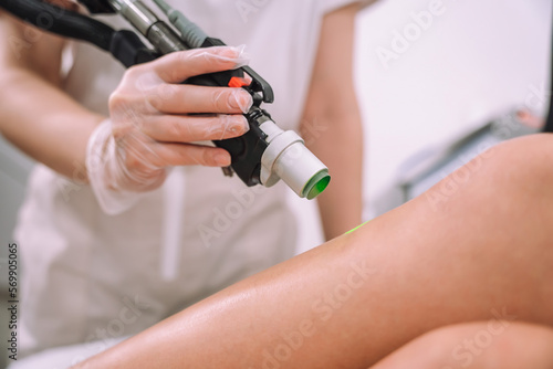 Close up shot of gloved hand with the laser hair removal machine's handpiece along woman leg. Alexandrite laser techhnology removing hair. Beauty procedure
