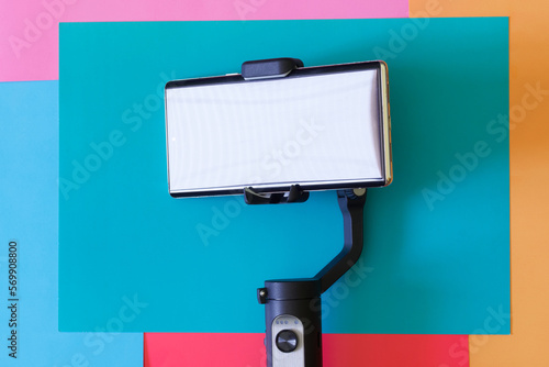 Modern mobile phone is a smartphone mounted on selfie stick - a gimbal, three-axis stabilizer for photo and video shooting. Gadgets for blogging and streaming. Colored background. photo