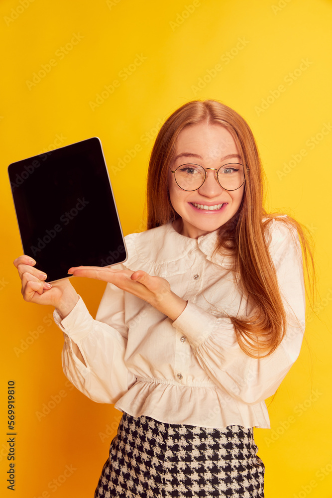 Happy young charming girl with red hair wearing office style clothes using tablet over yellow background. Concept of youth, student college life, business and education. Happy young charming girl with red hair wearing office style clothes using tablet over yellow background. Concept of youth, student college life, business and education.