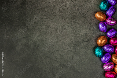 Delicious chocolate easter eggs ,sweets on dark black background,easter concept top view copy space wrapped colorful