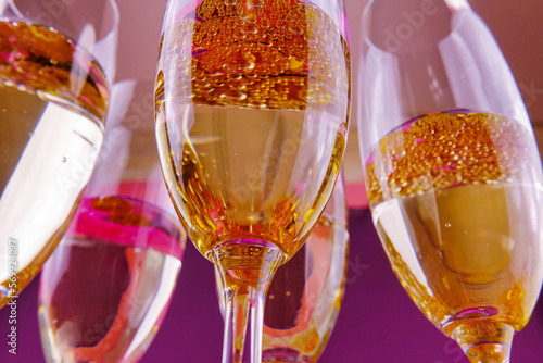 Wine glasses with sparkling wine on a lilac background and golden confetti.