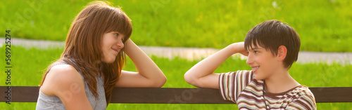 Foto Smiling teenage boy and girl sitting on the bench in the summer park