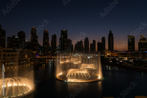 Dubai singing fountains at night lake view between skyscrapers. City skyline in dusk modern architecture in UAE capital downtown.