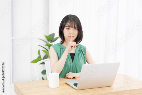 PCを使いながら口を指で押さえる若い女性