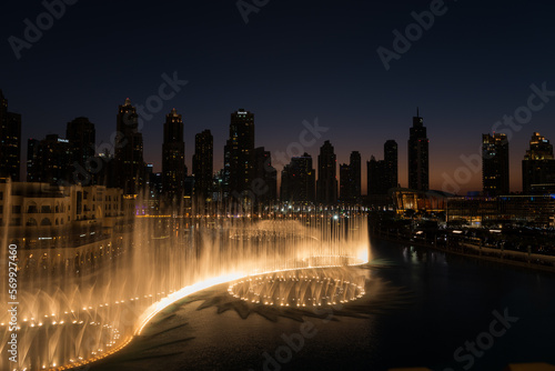 Dubai singing fountains at night lake view between skyscrapers. City skyline in dusk modern architecture in UAE capital downtown.