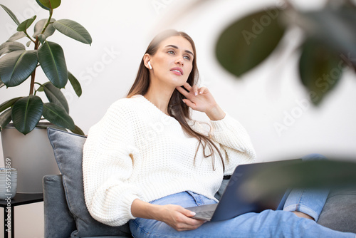 Fotografía A young woman sits thoughtfully on a sofa with a laptop on her lap