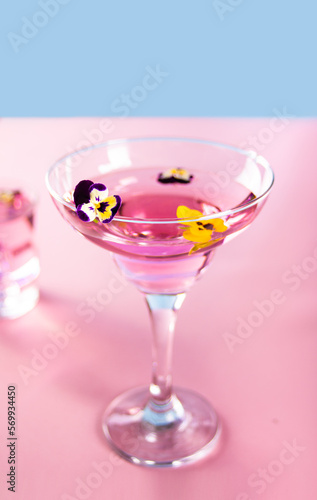 Glass of pink violet purple cocktail decorated flowers viola pancies