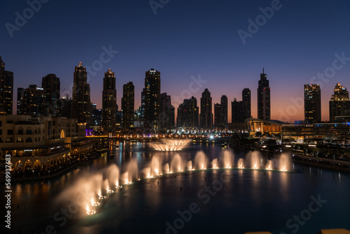 Dubai singing fountains at night lake view between skyscrapers. City skyline in dusk modern architecture in UAE capital downtown.