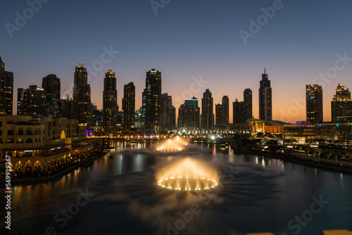 Dubai singing fountains at night lake view between skyscrapers. City skyline in dusk modern architecture in UAE capital downtown.