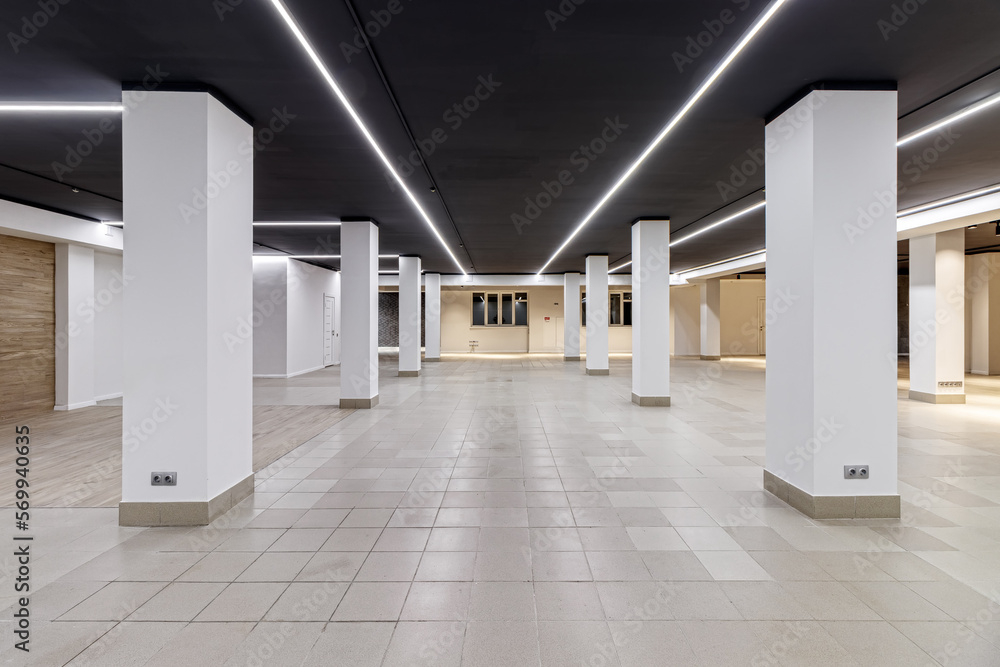 A large empty room with ceramic tiles on the floor, a black ceiling with lighting and columns propagating the ceiling