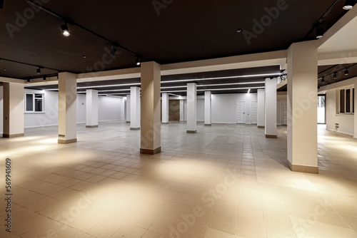 A large empty room with ceramic tiles on the floor, a black ceiling with lighting and columns propagating the ceiling photo