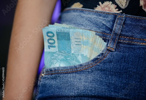 Cedula de reais no bolso com calça jeans com valor de 100 reais.