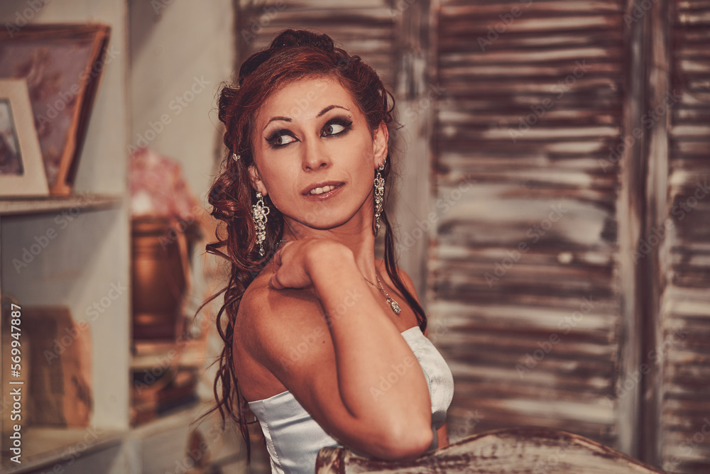 Fototapeta premium Wedding photos of the bride in a long, tight dress, with a bouquet of yellow orchids, with black arrows in her eyes, and curly red hair. Festive mood. A beautiful young girl is getting married.