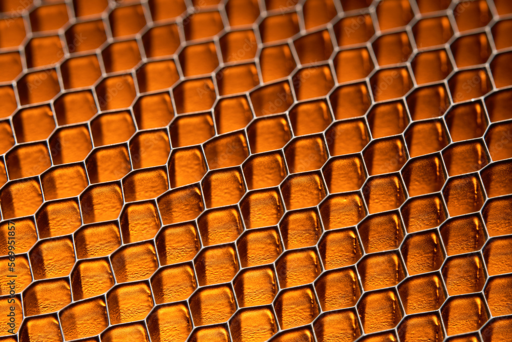 A pattern of metal grid cells in a golden yellow glow. Close-up macro shot.