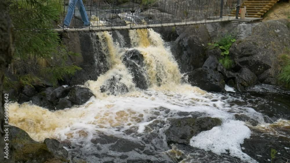 The suspension bridge is above the waterfall, people pass over the suspension bridge. The suspension bridge is above the waterfall, people pass over the suspension bridge.