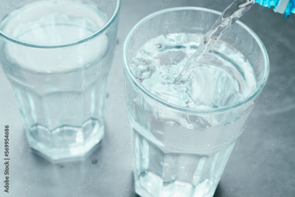 Pouring water from bottle into glass on grey background. Refreshing drink. Healthy lifestyle and stay hydrated Pouring water from bottle into glass on grey background. Refreshing drink. Healthy lifestyle and stay hydrated