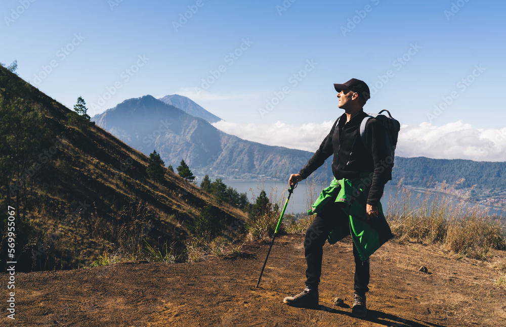 Traveling man leaning on trekking pole and admiring mountains in volcanic valley