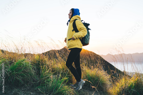 Smiling traveling woman standing on grassy mountain slope during trekking