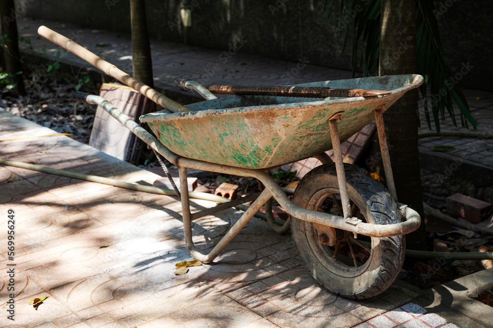 Dirty old wheelbarrow with tools in it left at a construction site. Mono wheel heavy-duty barrow with handles, contractors equipment Dirty old wheelbarrow with tools in it left at a construction site. Mono wheel heavy-duty barrow with handles, contractors equipment