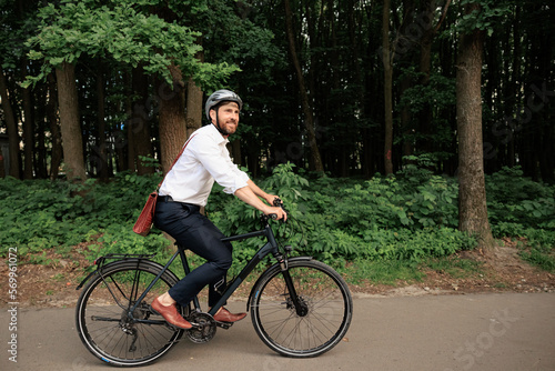 Fototapeta Naklejka Na Ścianę i Meble -  Dark haired businessman on bike, riding along park area outdoor.