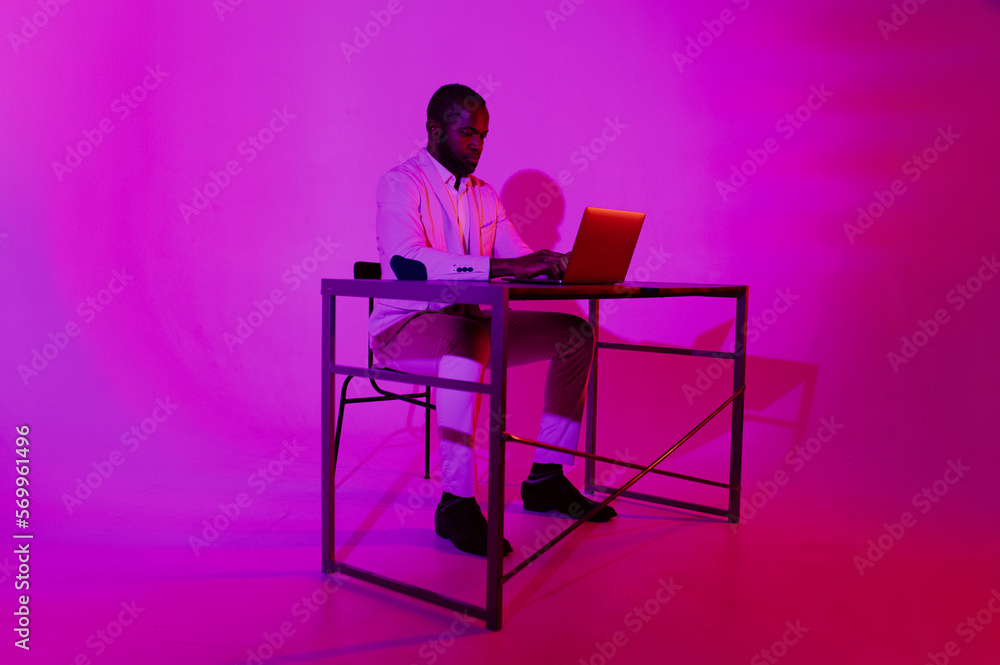 Fototapeta premium A man is sitting at a desk. A black programmer works using a laptop computer. the man works at night.