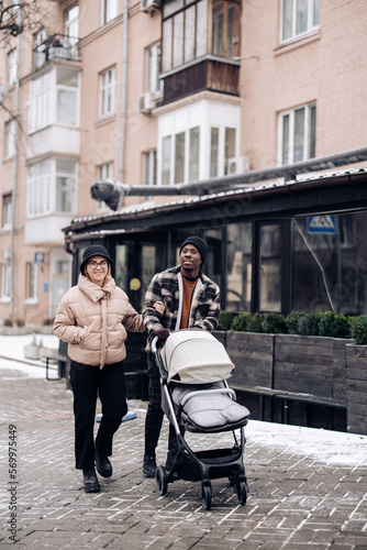 Happy interracial family walk on street and push baby carriage.