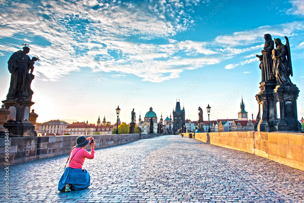 fascinating mystical landscape with a woman who makes a photo on Charles Bridge in an old city in Prague, Czech Republic at dawn. amazing places. popular tourist atraction