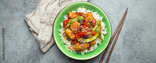 Asian sweet and sour sticky chicken with vegetables stir-fry and rice in ceramic bowl with chopsticks top view on gray rustic stone background, traditional Asian dish