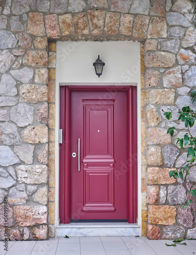 A reddish painted entrance door of a classic stone wall house. Travel to Athens, Greece. © Dimitrios
