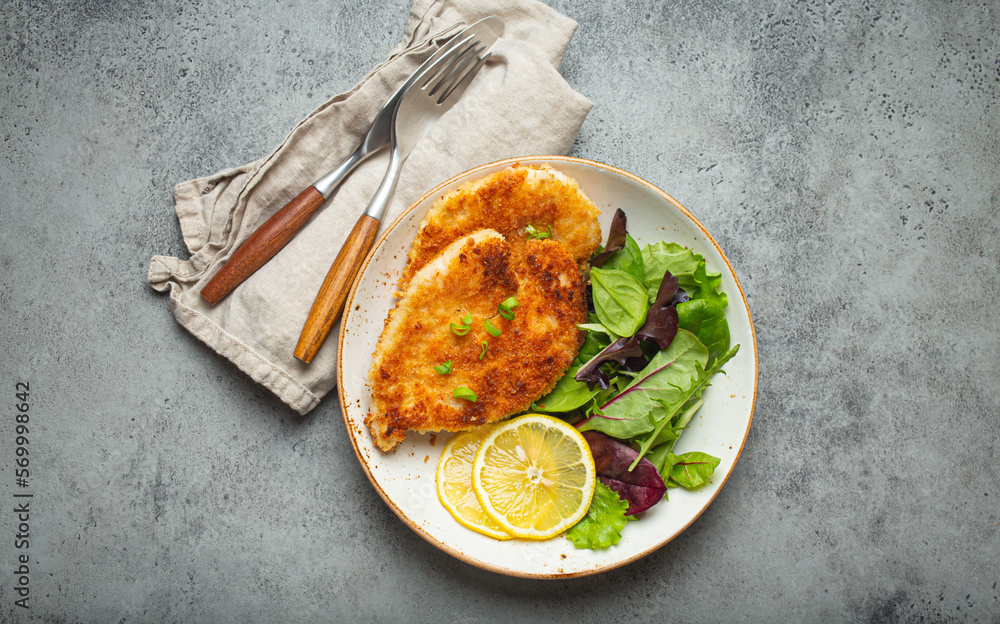 Crispy panko breaded fried chicken fillet with green salad and lemon on
