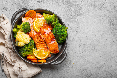 Valokuvatapetti Healthy baked fish salmon steaks, broccoli, cauliflower, carrot in black cast iron casserole bowl on grey stone background