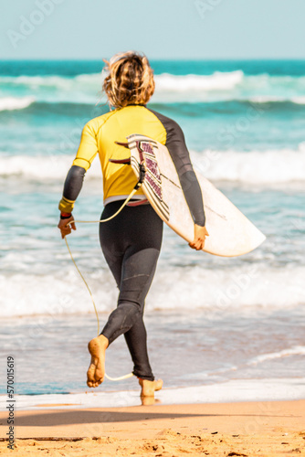 Foto surfer with yellow lycra and a shortboard running by the beach to catch waves an